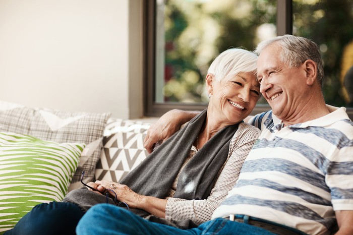 A senior couple sitting on the couch and smiling.
