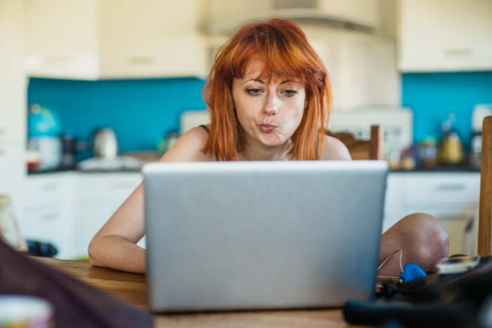 Woman sitting in kitchen and staring intently at laptop screen